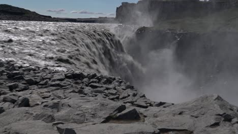 Zoom-out-shot-of-strong-Dettifoss-Waterfall-crashing-down-rocky-edge-during-sunny-day-in-Iceland