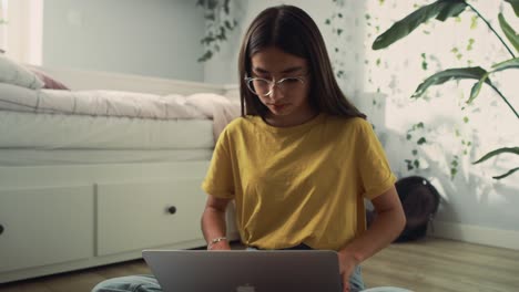 zoom out of caucasian teenage girl sitting on floor and using laptop to learn