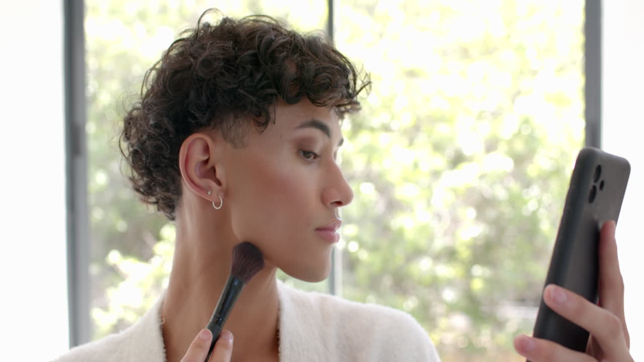 Applying makeup, non binary person using smartphone as mirror at home