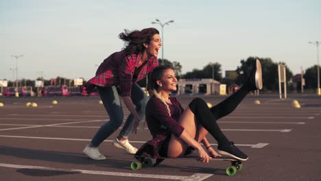 smiling woman sitting on a longboard while her friend is pushing her behind and running during sunset