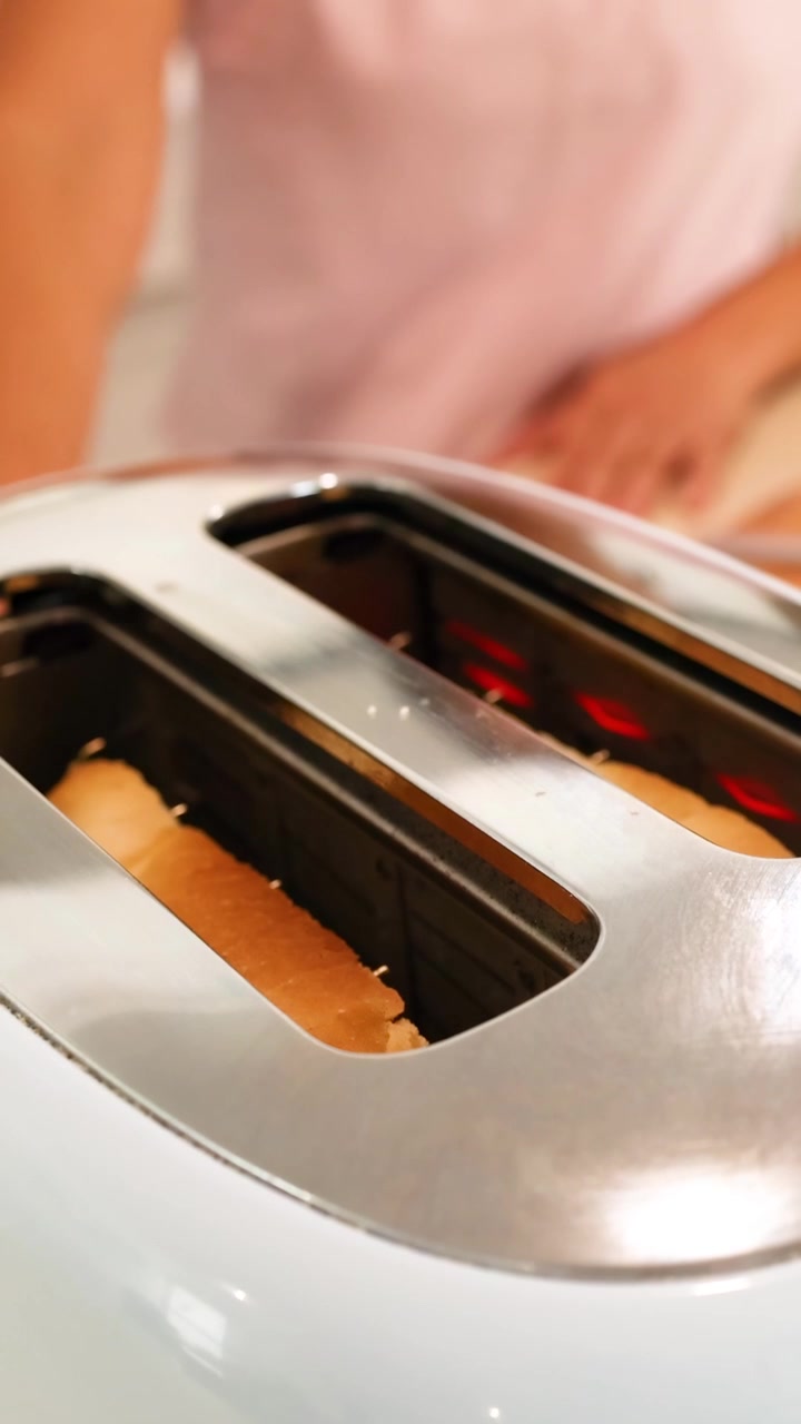 A person toasts bread in a sleek toaster, with warm lighting creating a cozy kitchen atmosphere