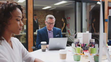 Businessman-And-Businesswoman-Working-On-Computers-In-Open-Plan-Office-With-Colleagues-In-Background