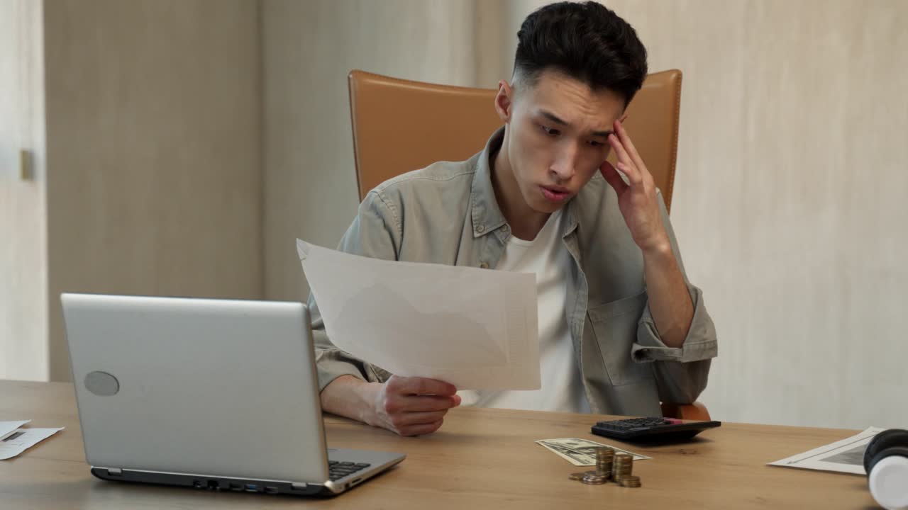 젊은 아시아인 남자가 계산기로 돈을 세고 신문을 찾습니다.