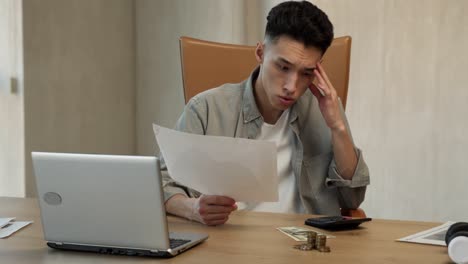joven asiático cuenta dinero en la calculadora mirando los papeles
