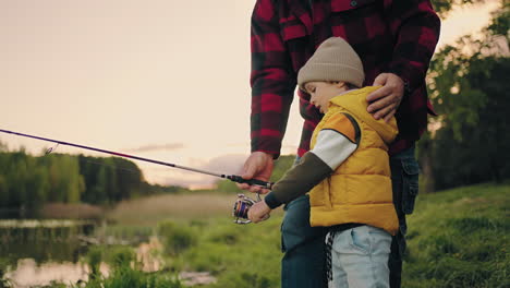 grandfather-and-little-boy-are-resting-on-shore-of-lake-and-fishing-rest-in-nature-in-spring-or-summer