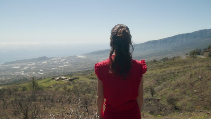 Young woman tourist in red dress looking at dry landscape of southern Tenerife, Canary Islands in spring