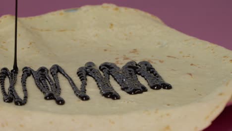 pouring melted chocolate over a crepe