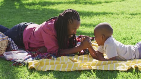 video of happy african american father and son having picnic on grass, arm wrestling