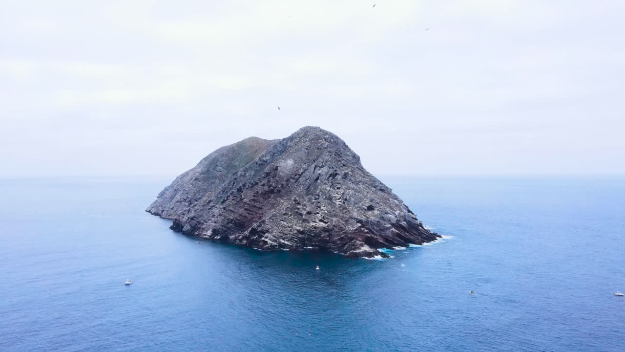 Aerial pullback rises above Coronado Islands, Mexico, with focus on the rugged coastline and distant mountain backdrop centered in harmony