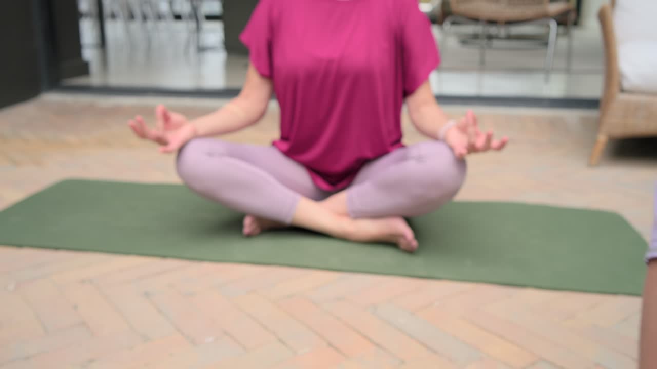 Amigos haciendo yoga en colchonetas verdes en el patio, la cámara se aleja revelando a una mujer con pulsera negra sonriendo