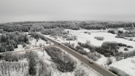 aerial view of a two lane highway in countryside with cars passing by. asphalt road intersection with gravel road. frost over the landscape in winter season.