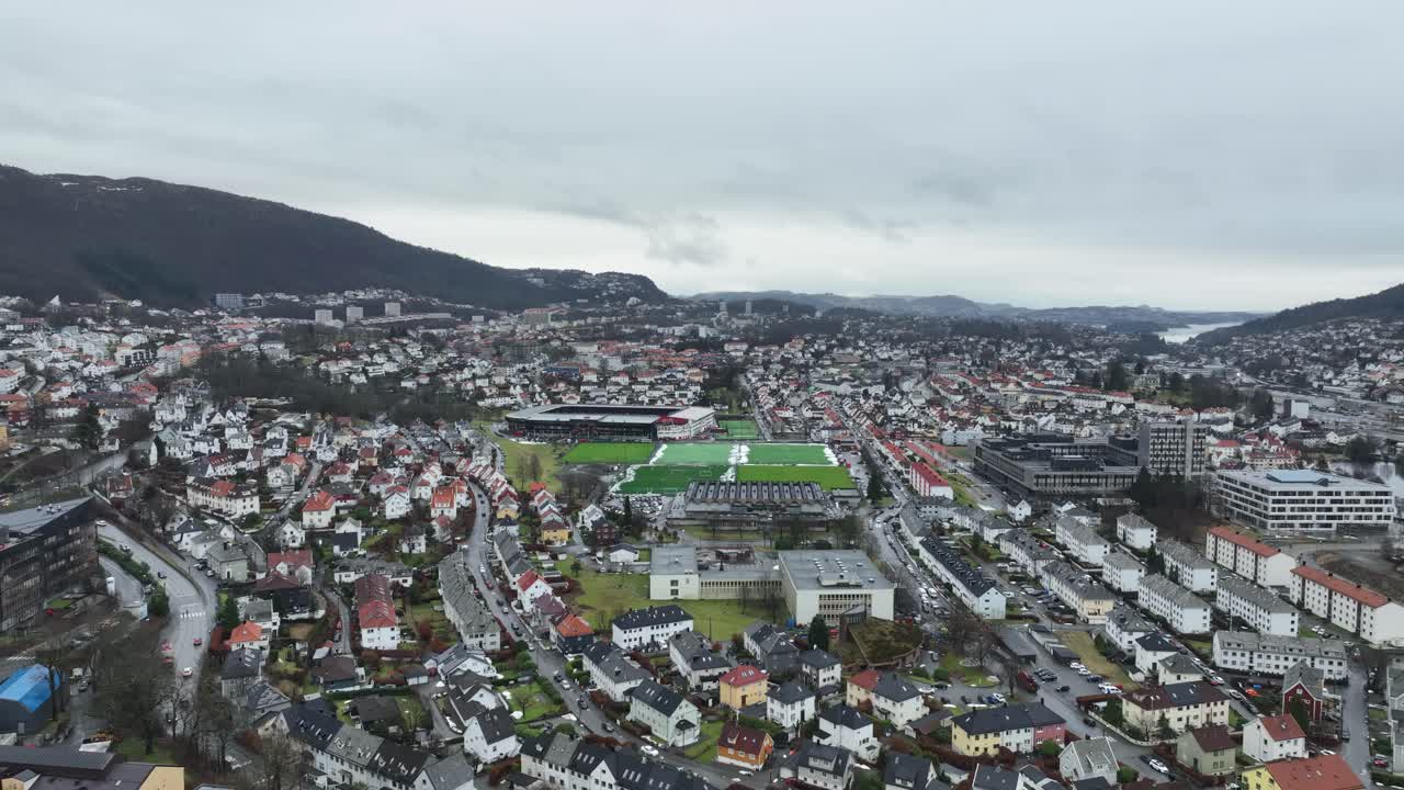 Descending aerial facing Brann soccer stadium in Bergen, Minde and Arstad areas with dense buildings. Overcast winter, no snow