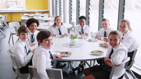 retrato de estudiantes de secundaria vestidos con uniforme sentados alrededor de la mesa y comiendo almuerzo en la cafetería