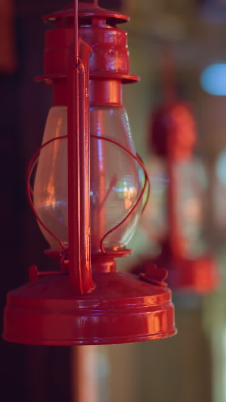 Close-up view of a vintage red lantern hanging on a wooden beam with a blurred background, creating a warm and rustic ambiance
