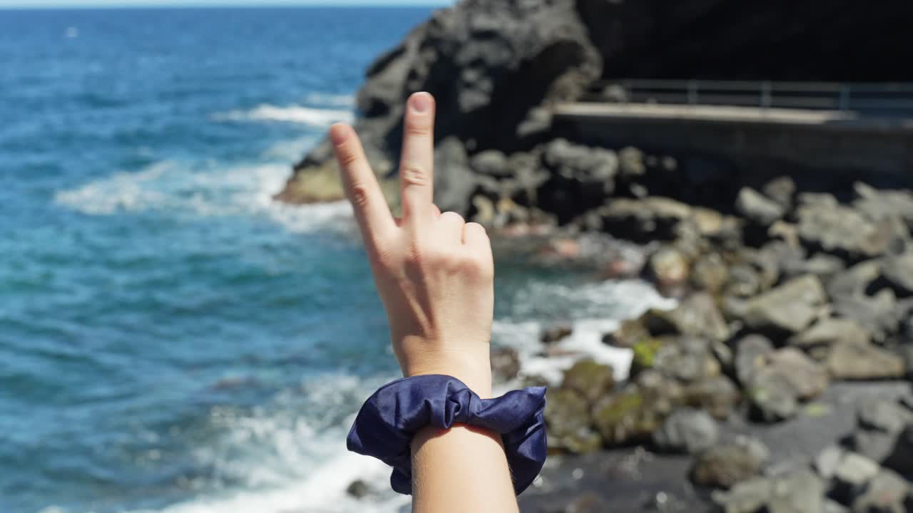 la mano de la mujer sosteniendo un signo de paz con los dedos en el fondo de la costa del océano tropical