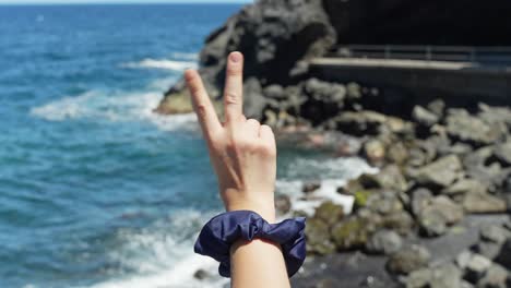 female's hand holding peace sign with fingers on tropical ocean coast background