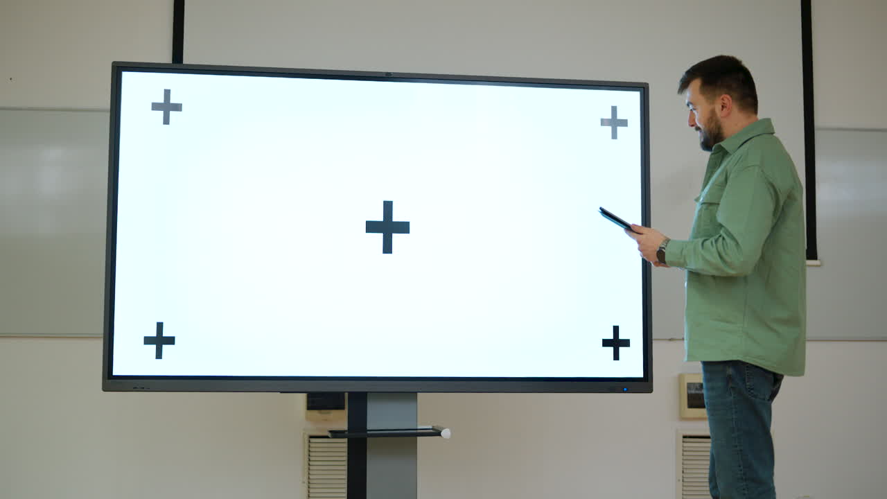 Man presenting in a spacious classroom using a large screen with a whitescreen and tracking points, ichroma key ready