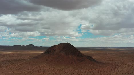 A-cone-shaped-mountain-towers-over-the-Mojave-Desert-landscape-on-an-overcast-day---orbiting-aerial-view