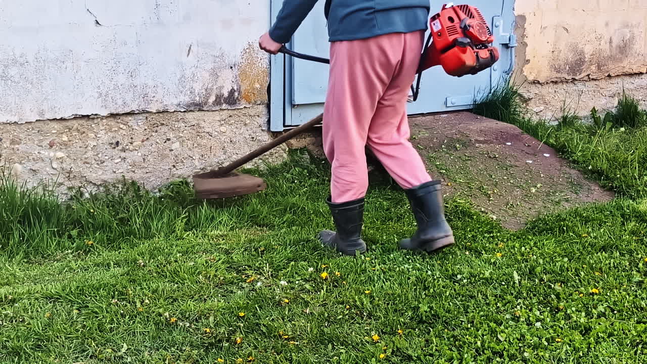 Person Cutting Grass Around Her House With A Grass Cutter Machine. - crop shot