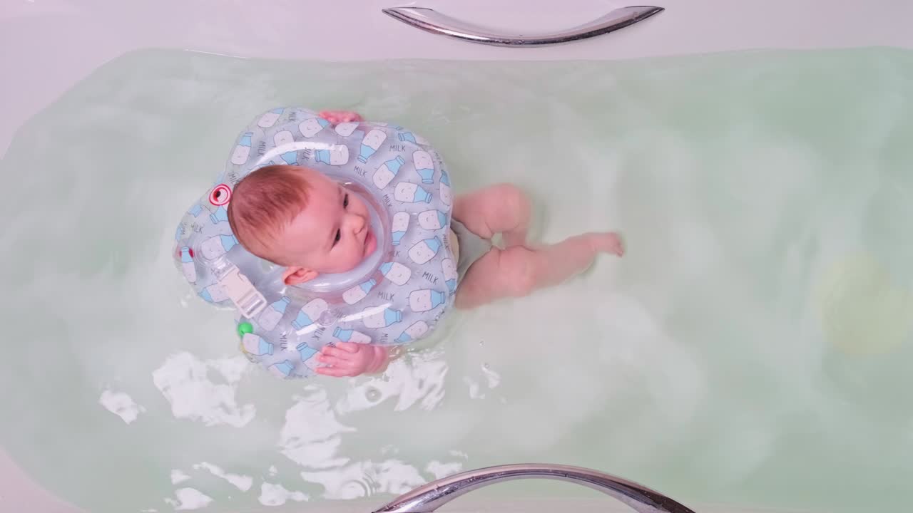 목에 고무 반지를 달고 욕조에서 수영하는 동안 웃는 행복한 아기 아기.