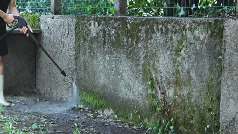 man using electric powered pressure washer to power wash dirty wall