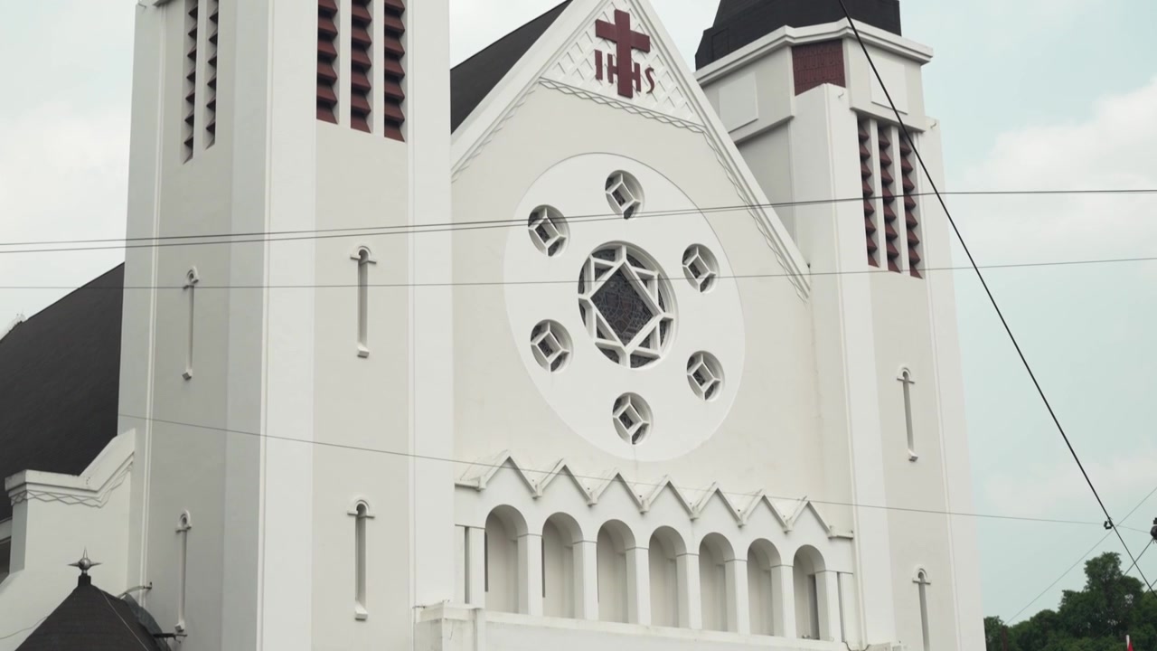 Panorâmica ascendente da fachada da catedral com bandeiras indonésias e torres de relógio gêmeas em Malang