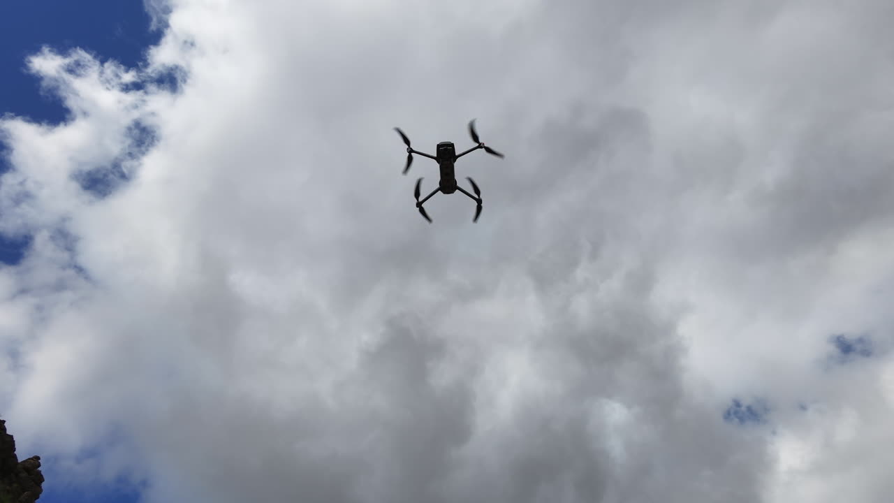 Silhouetted drone performing agile aerial freestyle maneuvers against a cloudy blue sky