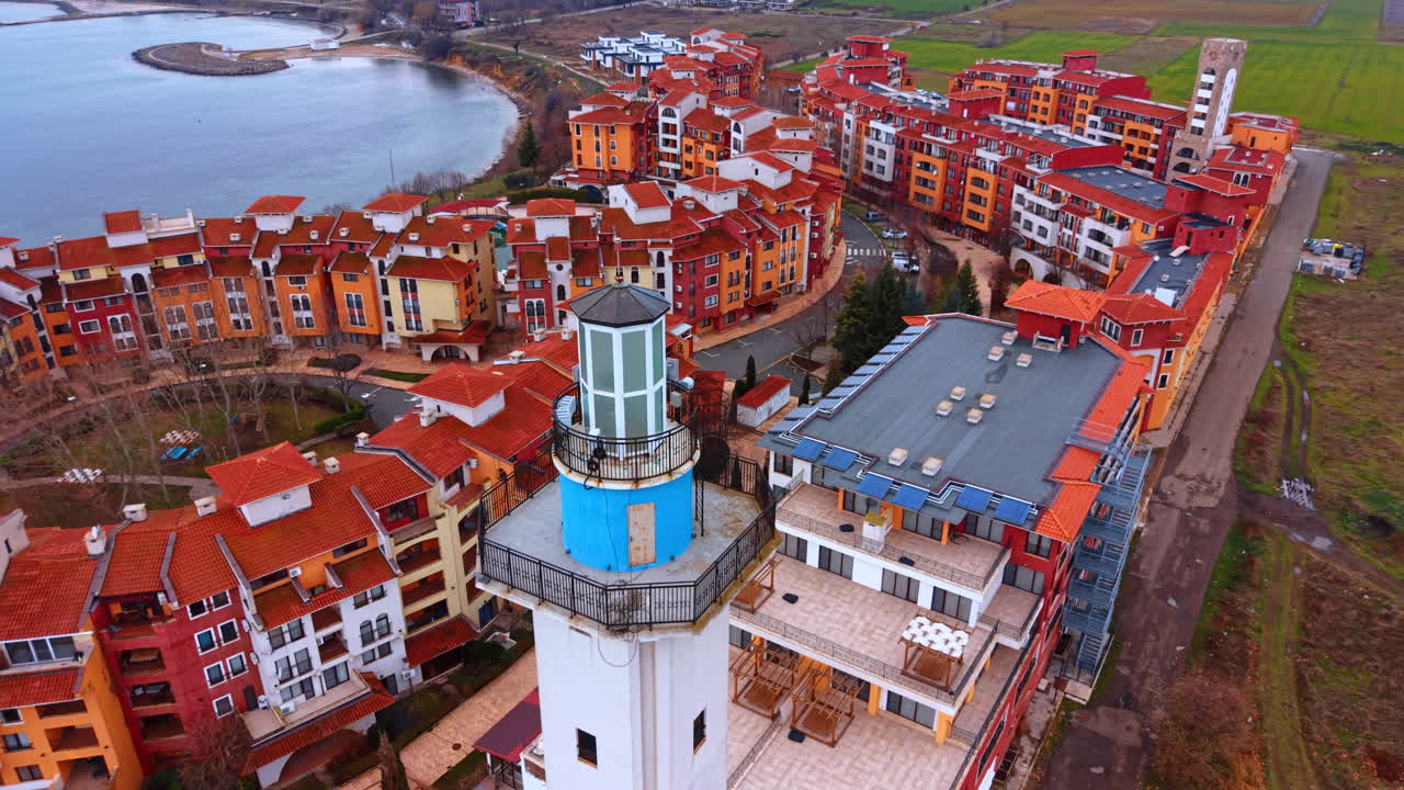 Vista dall'alto di un locale lanterna di un faro e tetti. Inquadratura dall'alto della parte superiore di un faro con un locale lanterna blu accanto a tetti in tegole rosse e campi verdi.