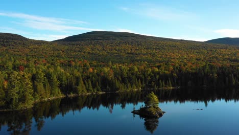 aerial drone shot over a calm forest lake with a small island and thick green forest into the distance of the maine wilderness