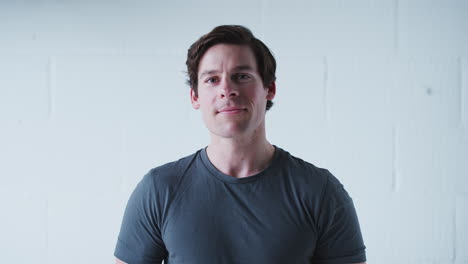 portrait of smiling man wearing t shirt standing against white studio wall