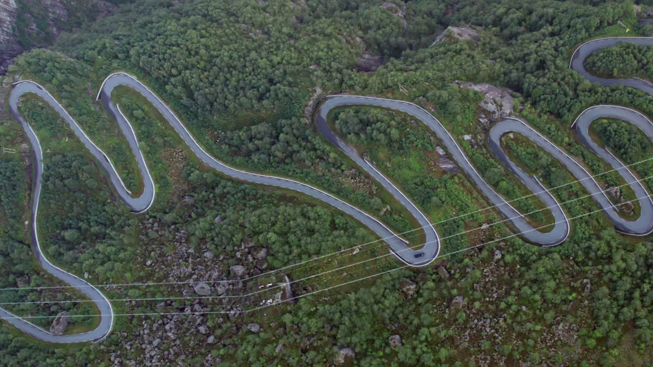 vista aérea cercana de arriba hacia abajo de una carretera serpenteante estrecha y tortuosa mientras serpentea por un lado empinado y cubierto de bosque del valle, junto a un fiordo en noruega