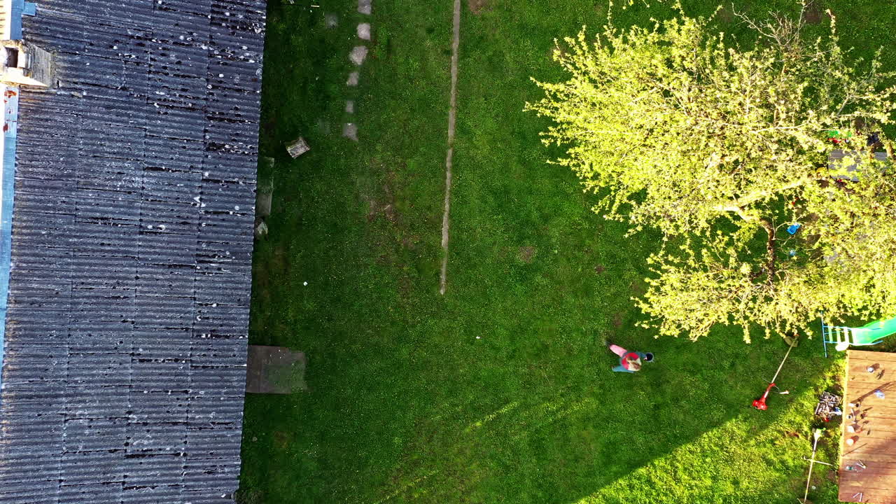 Aerial view of woman walking across yard to a brush cutter laying in grass