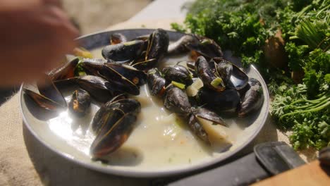 a plate of fresh mussels on a sunny day in the summer while a person grabs one mussel to eat