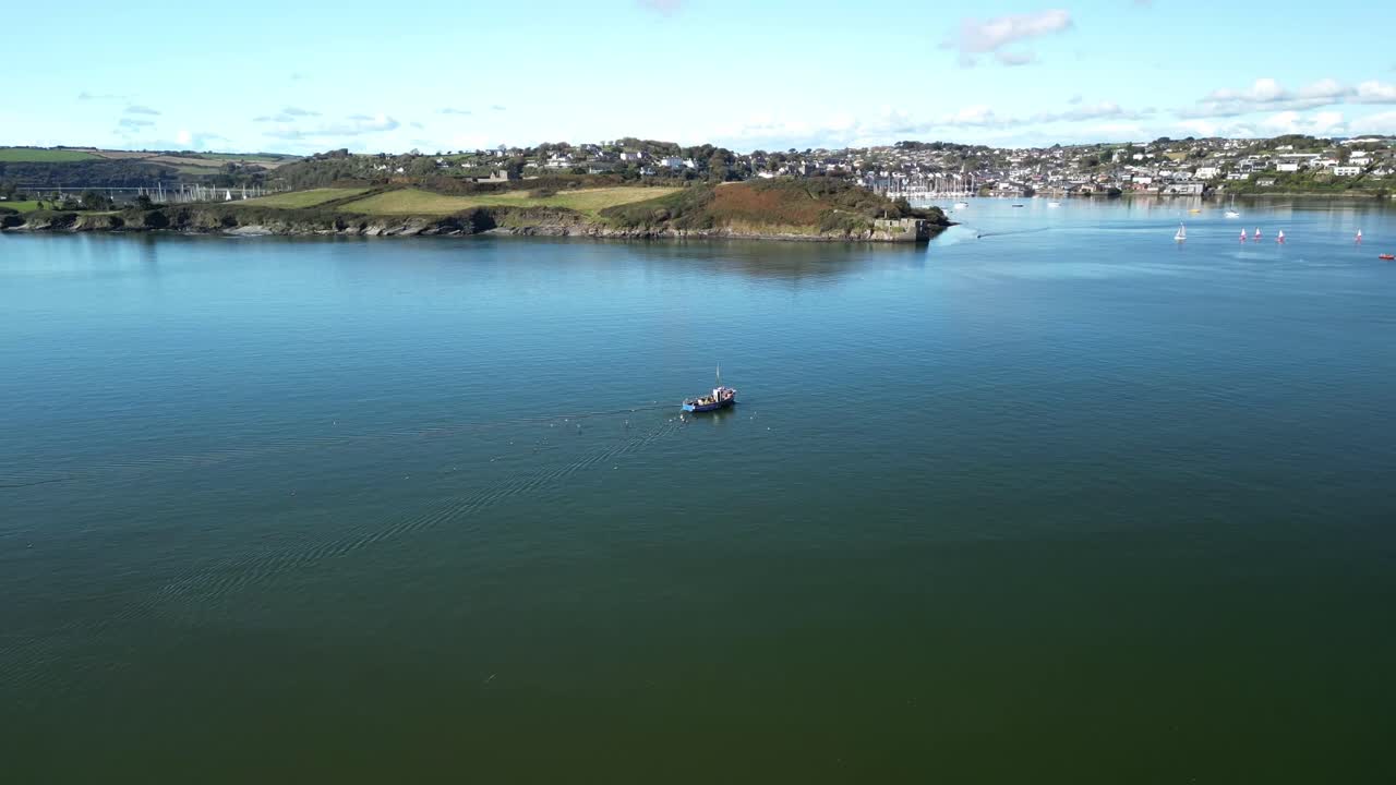 Coastal Ireland from above with drone follow fishing boat with flock of seabirds heading into harbour. Sunny, green waters of Kinsale.