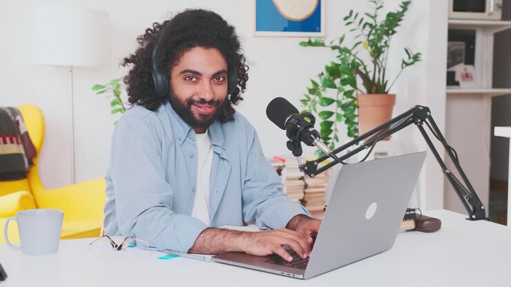 Young arabian man types email on laptop sits at table with microphone in office