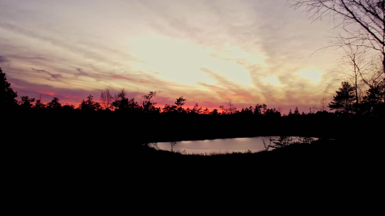 el cielo dorado de la puesta de sol se refleja en el estanque congelado con la silueta de los árboles alrededor