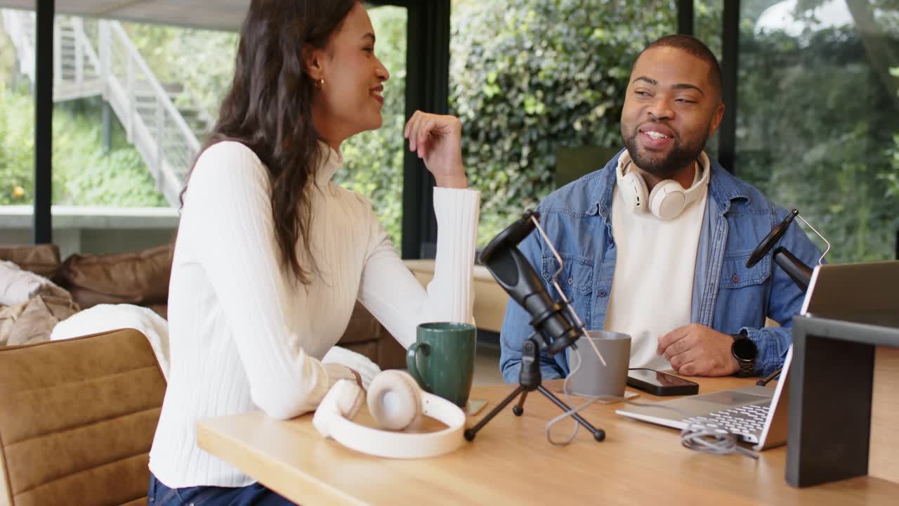 Reacting to shared joke, Diverse cohosts laughing and gesturing into microphone at studio table