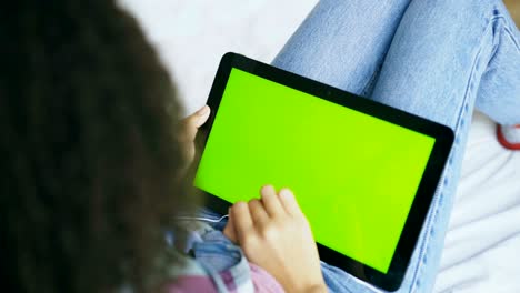 vista trasera de una mujer rizada en casa usando una tableta electrónica con pantalla verde