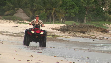 a man rides an atv through the water on the beach