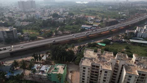 a service road, quickly moving cars, and residential and commercial buildings on an expanding indian highway are all depicted in dramatic aerial footage