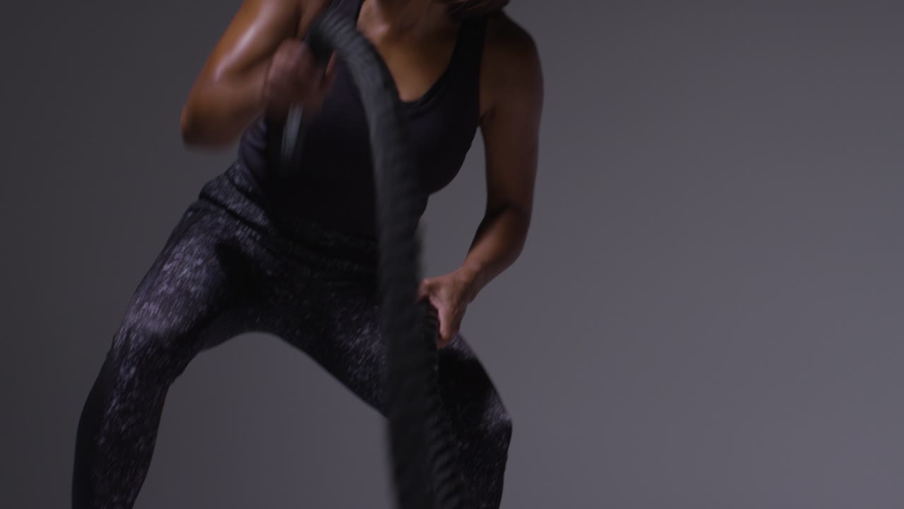 운동복을 입은 성숙한 여성이 전투 로프 3로 심장 운동을 하는 클로즈업 스튜디오