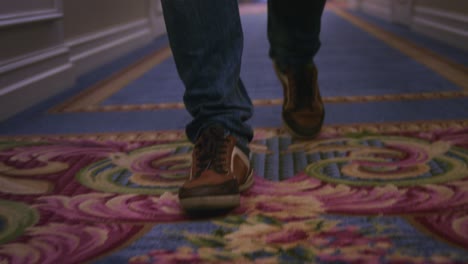 man legs in brown sneakers walking on blue carpet on long corrido