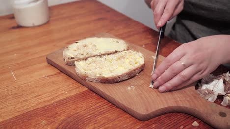 las manos de la mujer ponen ajo en una segunda rebanada de pan con mantequilla