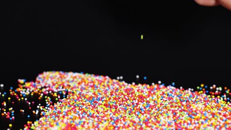 hand touching colorful sprinkles on a black surface