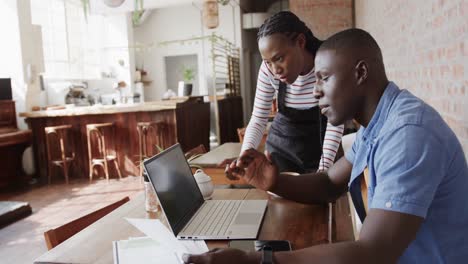 Serious-african-american-male-and-female-coffee-shop-owners-using-laptop-and-talking,-slow-motion