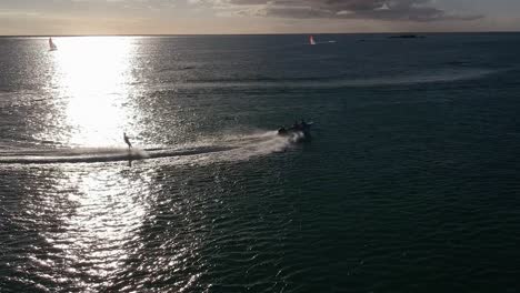 Toma-Aérea-De-Un-Esquiador-Acuático-Que-Describe-Una-Curva-Por-Delante-Del-Reflejo-Del-Agua-Del-Sol-Al-Atardecer