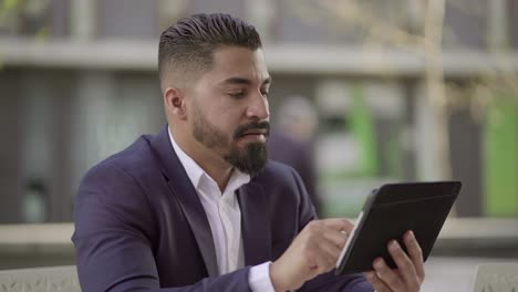 Serious handsome businessman using tablet pc outdoor