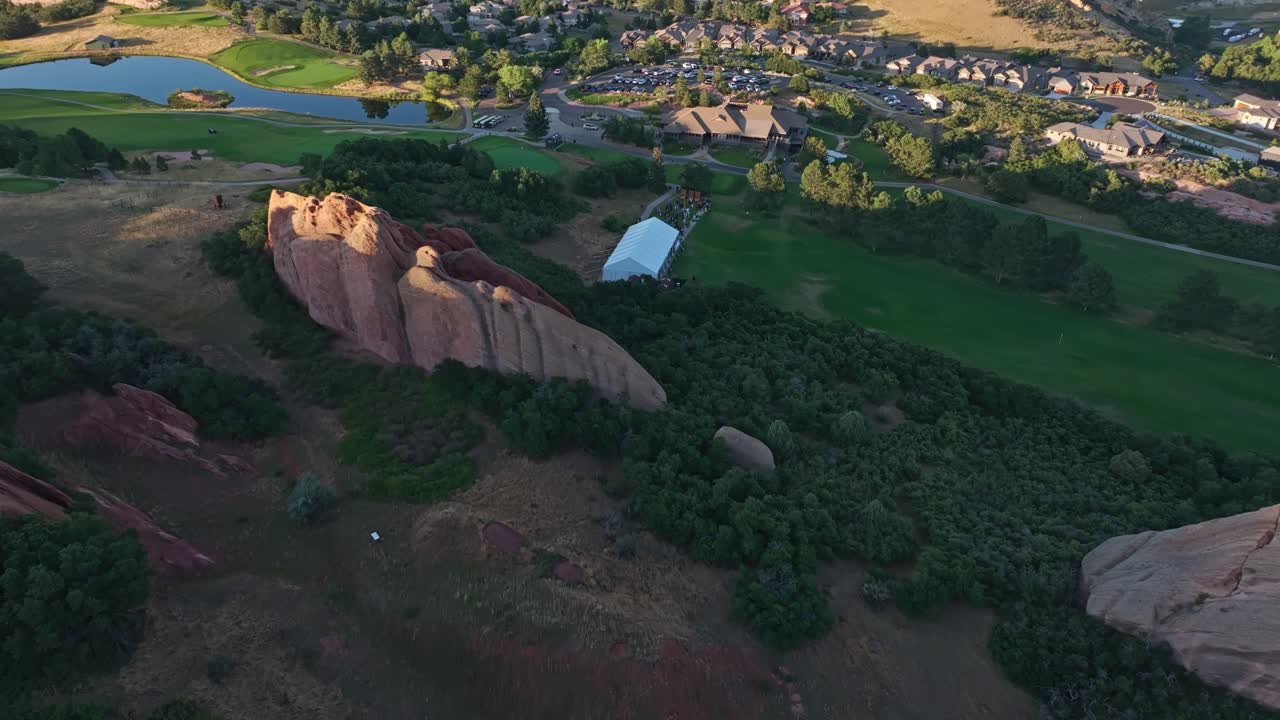 Drone ascends tilting down over golf course nestled among red rock ridges and green terrain in summer, Arrowhead jagged rocks and venue