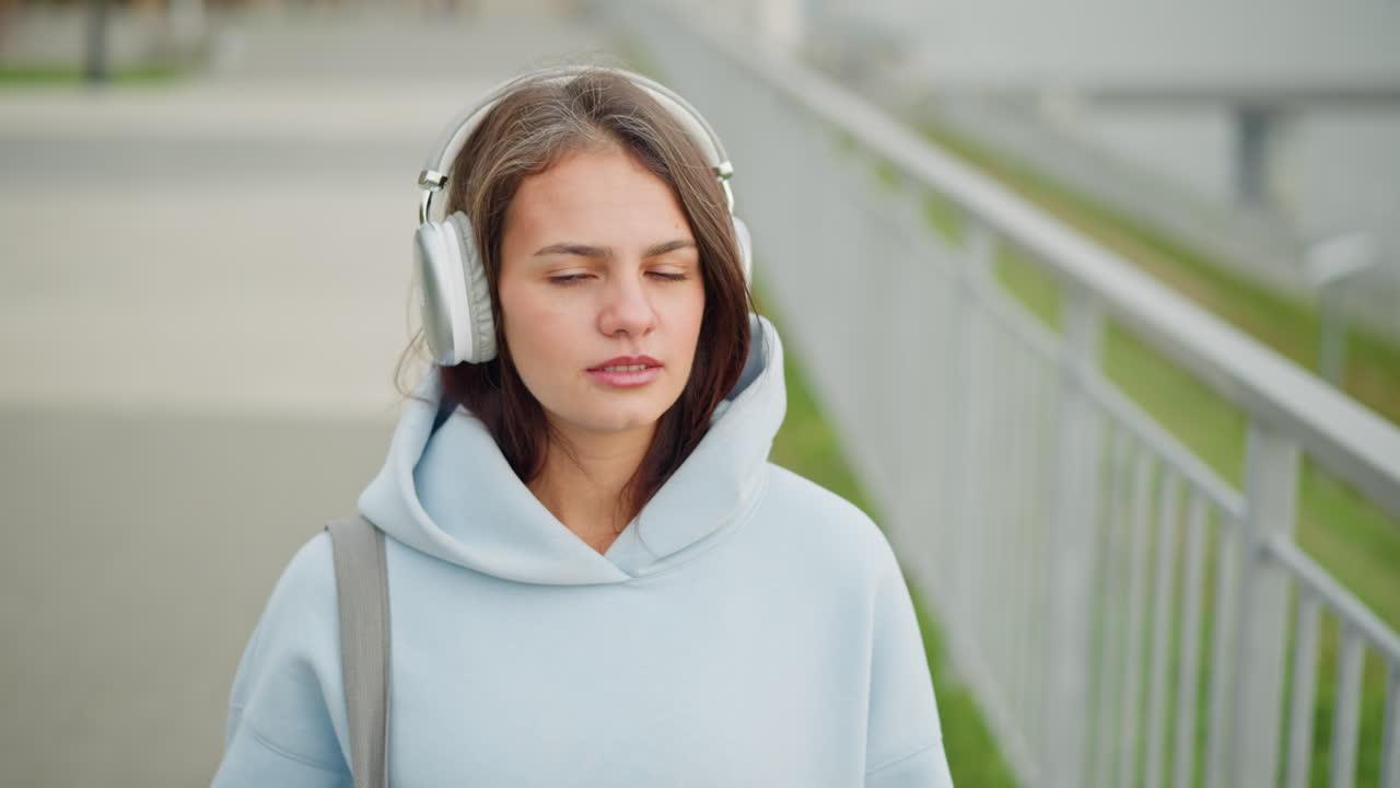 Close-up view of pretty lady smiling, walking in a calm environment while listening to music with headphones, peaceful stroll in an outdoor setting with a relaxed vibe
