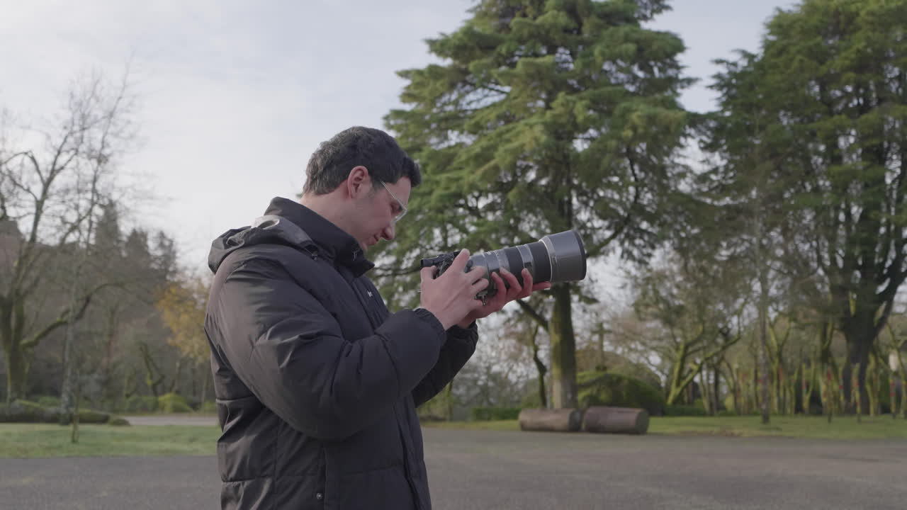 Photographer reviews camera with telephoto lens while standing outdoors
